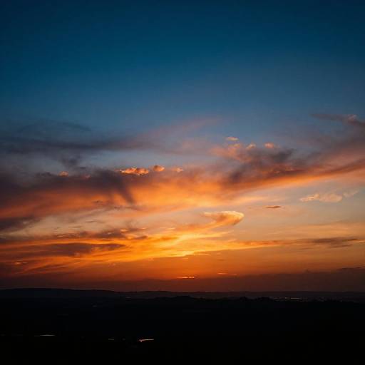 Photograph of a vibrant sunset with deep blue sky, orange and yellow clouds, and a dark horizon. Rich colors contrast against the evening light.