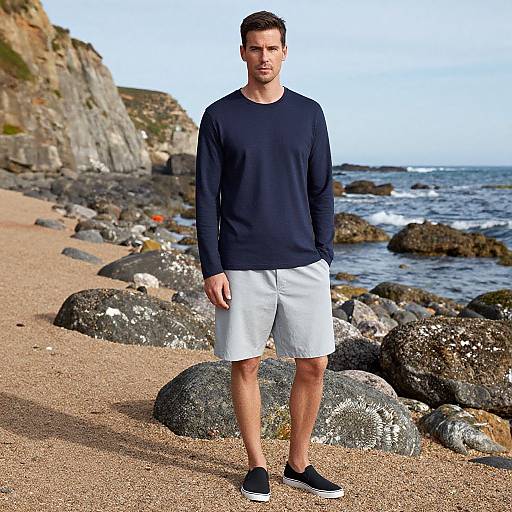 Photograph of a handsome man with short brown hair, wearing a navy long-sleeve shirt, white shorts, and black sneakers, standing on a