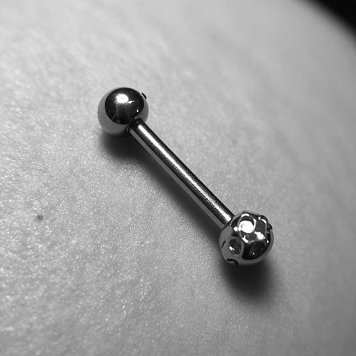 Close-up photograph of a shiny, silver-colored ball-end pin laying on a textured, silver-gray surface, highlighted by focused lighting.