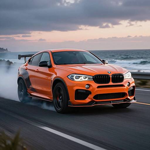 Photograph of an orange BMW M4 sports car with black wheels, driving on a coastal road, emitting smoke, under a cloudy sunset sky.