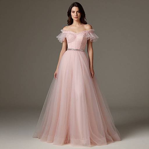 Photograph of a brunette woman in an off-shoulder, pastel pink, lace bodice ball gown with a tulle skirt, standing against