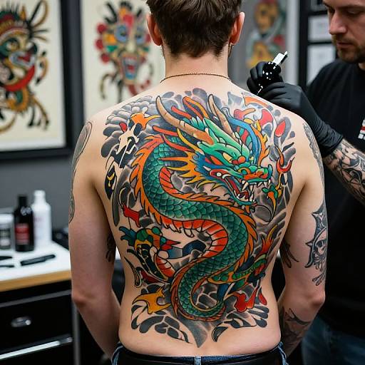 Photograph of a man's back with a vibrant, colorful dragon tattoo covering his entire upper back, being touched by a tattoo artist in a tattoo par
