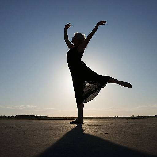 Silhouetted dancer in flowing dress, arms raised, sun behind, casting long shadow, against clear blue sky, on expansive open ground.