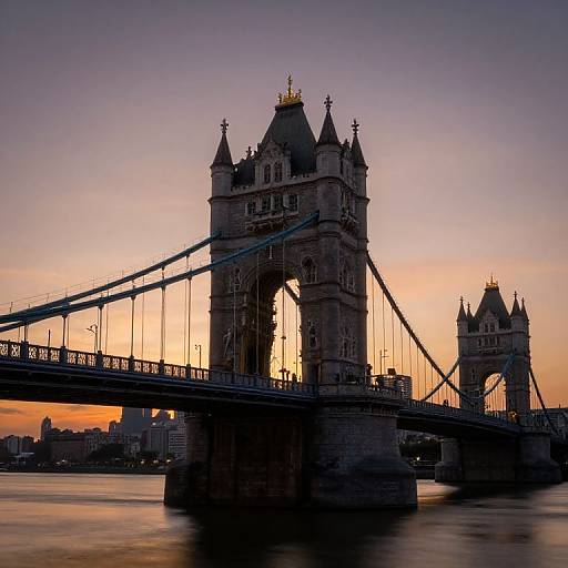 Photograph of London's Tower Bridge at sunset, silhouetted against a pink and purple sky, with the Thames River in the foreground.
