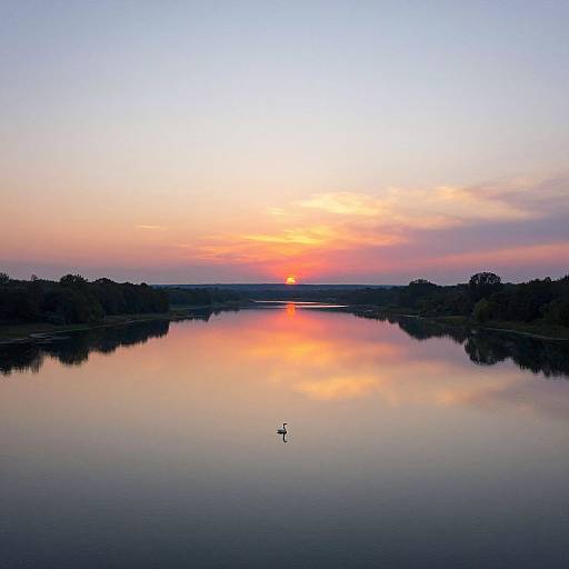 Photograph of a serene lake at sunset, reflecting vibrant orange and pink sky, with a single bird in the center.