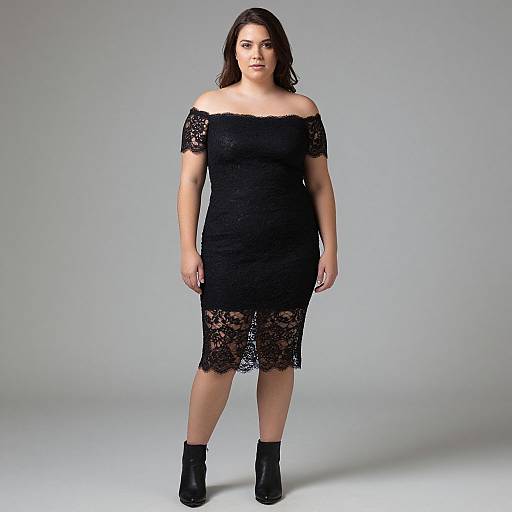 Photograph of a curvy woman with medium skin tone, wearing an off-the-shoulder, black lace dress and black ankle boots, standing against
