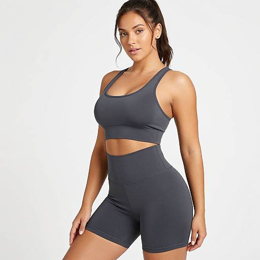 Photograph of a fit, tan-skinned woman with dark hair in a ponytail, wearing a dark blue sports bra and matching high-waisted