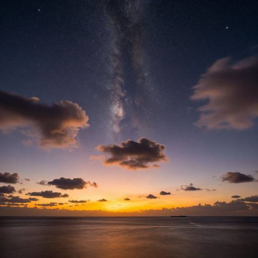 Photograph of a stunning twilight sky, with the Milky Way galaxy prominently visible above scattered, pink-hued clouds against a gradient of orange, yellow,