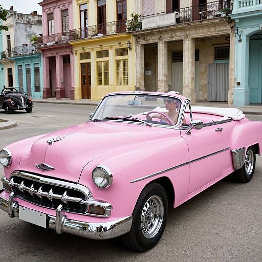 Photograph of a vintage pink convertible car with chrome details, parked on a street in front of colorful, colonial-style buildings.