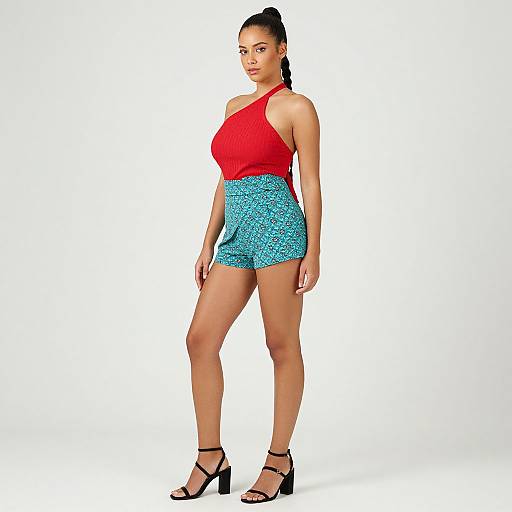 Photograph of a tall, fit woman with dark hair in a ponytail, wearing a red sleeveless top, blue patterned shorts, and black