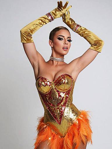 Photograph of a glamorous woman with fair skin, wearing a gold and orange sequined corset with feather skirt, long gold gloves, and choker