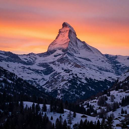 Photograph of a snow-capped mountain peak at sunset, with vibrant orange and pink sky, dark evergreen trees in the foreground.