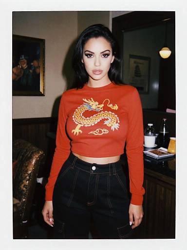 Photograph of a young woman with long black hair, wearing a red long-sleeve crop top with a yellow dragon design, and black high-w