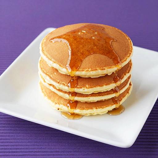 Photograph of a stack of four golden-brown pancakes with syrup, on a white square plate, against a purple textured background.