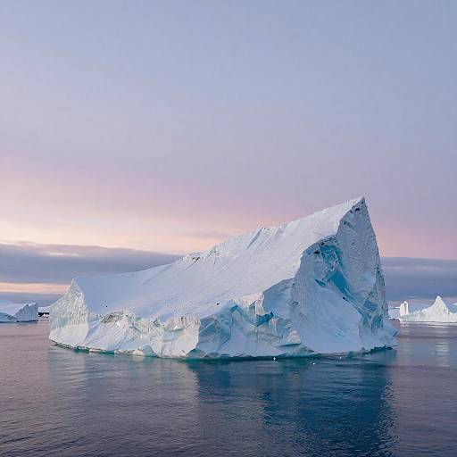 Photograph of a large, jagged icebergs floating in calm, dark blue ocean water under a pastel pink and blue twilight sky.