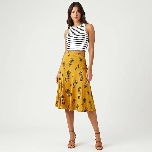 Photograph of a young woman with dark hair, wearing a white and black striped crop top, yellow pineapple-patterned skirt, and beige sandals, standing