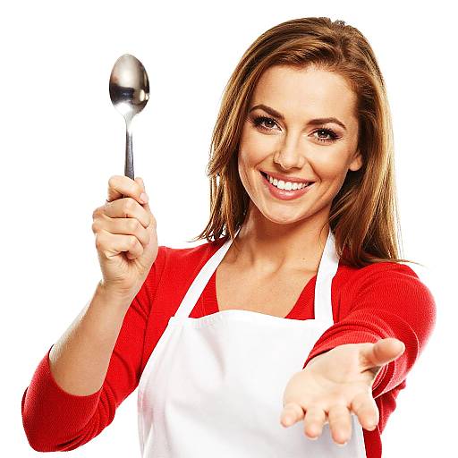 Photograph of a smiling, brown-haired woman in a red top and white apron, holding a spoon and extending her hand forward against a white background