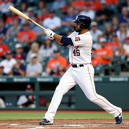 Photograph of a baseball player in white uniform, number 46, mid-swing, with blurred crowd in red and gray in background.