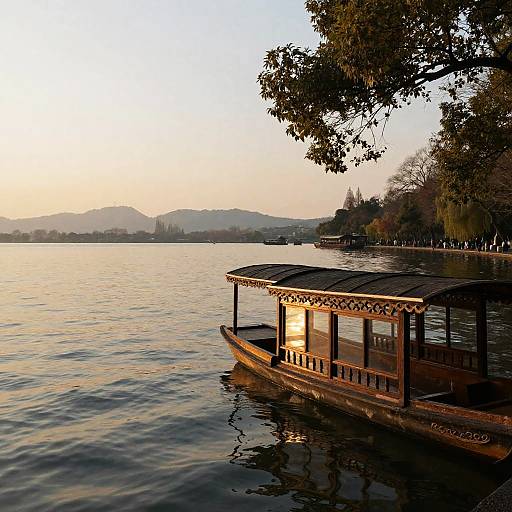 Photograph of a wooden boat with a roofed platform floating on a calm lake at sunset, trees in the background, mountains on the horizon.