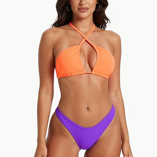 Photograph of a tan-skinned woman with wavy dark hair, wearing an orange halter bikini top and purple bikini bottoms, standing against a white
