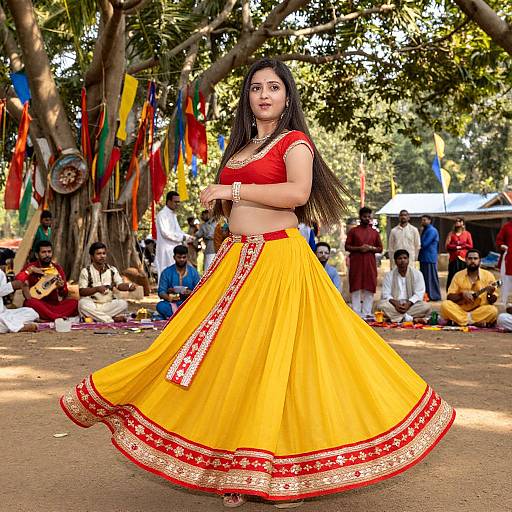 Photograph of a South Asian woman in a red top and yellow skirt with red and gold trim, dancing outdoors in a tree-shaded festival setting,