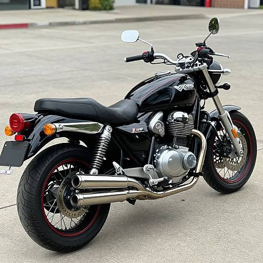 Photograph of a black, vintage-style motorcycle with chrome accents, black leather seat, and red-tipped tires, parked on a concrete street.