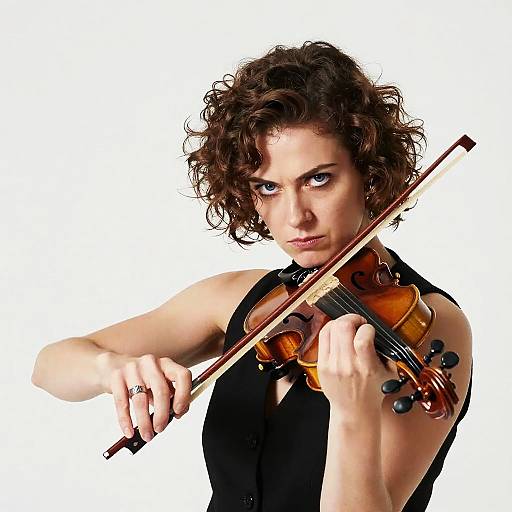 Photograph of a curly-haired woman with intense gaze, playing a violin against a white background, wearing a black sleeveless top.