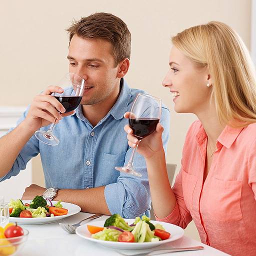 Photograph of a smiling Caucasian couple with short brown hair and blonde hair, wearing blue and coral shirts, sipping red wine at a table with colorful