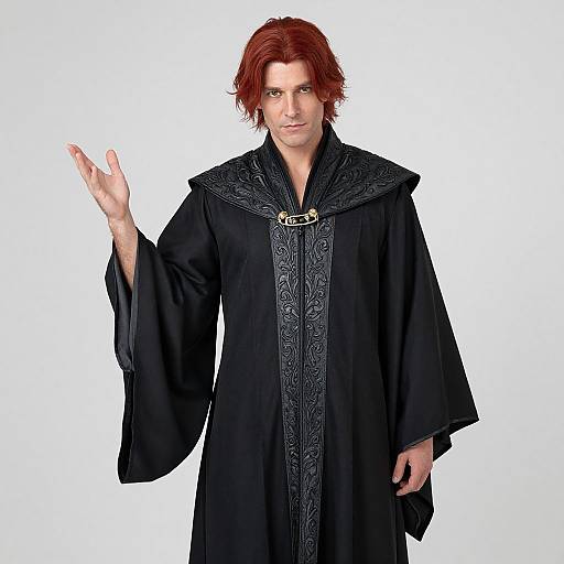 Photograph of a red-haired man with pale skin, wearing a black, ornately-embroidered, medieval-style robe, raising his right hand