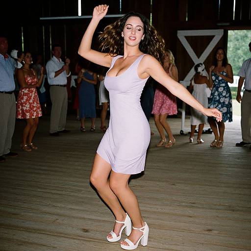 Photograph of a smiling, brunette woman in a white, sleeveless dress and white high heels dancing indoors, surrounded by a diverse, casually dressed group