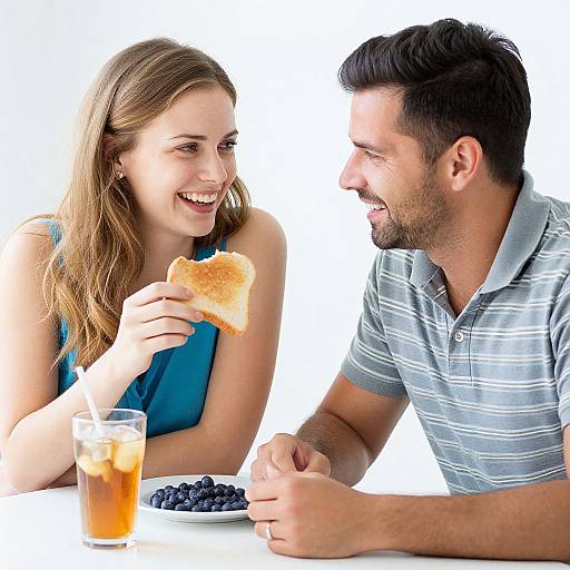 Photograph of a smiling couple with light brown hair and dark hair, eating toast and blueberries, with a glass of iced tea.
