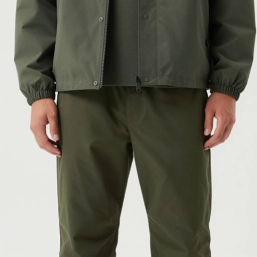 Photograph of a person's torso in black jacket and green pants, hands at sides, against a plain white background.