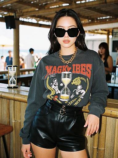 Photograph of a woman with long black hair, wearing black sunglasses, gold chain necklace, black 