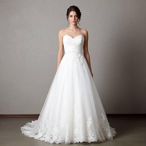 Photograph of a fair-skinned woman with dark hair in an elegant, strapless, white lace wedding gown, standing against a plain gray background.