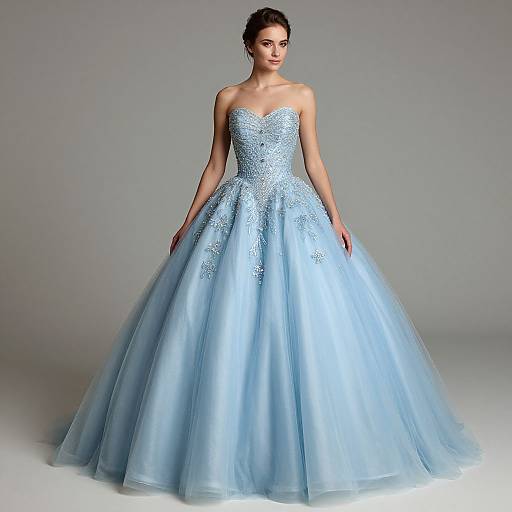Photograph of a woman in a strapless, light blue, intricately beaded ball gown with a voluminous tulle skirt, standing against a