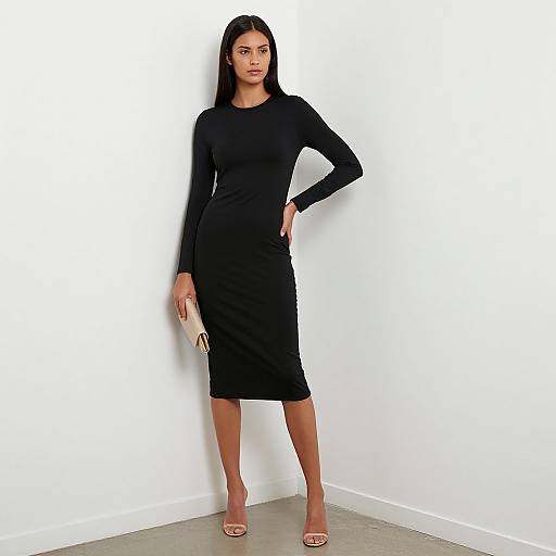 Photograph of a confident woman with long black hair, wearing a fitted black long-sleeve dress, holding a gold clutch, standing against a white