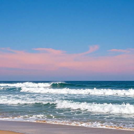 Photograph of a beach at sunset with vibrant blue sky, pink clouds, crashing white-capped waves, and golden sand in the foreground.