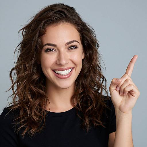 Photograph of a smiling woman with wavy dark brown hair, fair skin, and brown eyes, wearing a black shirt, pointing upward with her right