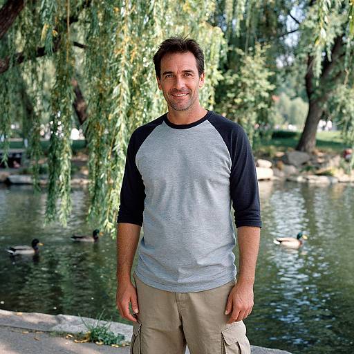 Photograph of a smiling man with short dark hair, wearing a black-and-gray raglan shirt and beige cargo pants, standing in a park with a