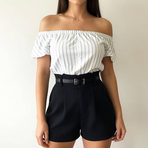 Photograph of a woman with long dark hair, wearing an off-shoulder white striped top and high-waisted black shorts, standing against a