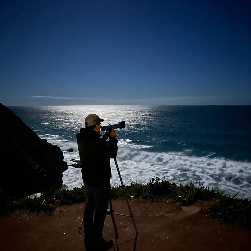 Photograph of a silhouetted photographer with a camera on a tripod, capturing a sunlit ocean scene with dark, crashing waves.