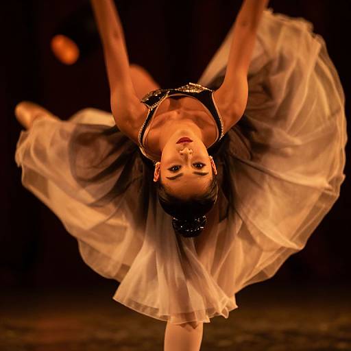 Photograph of a ballerina, upside down, in a dramatic, backlit pose with a flowing, white tutu and black top, against