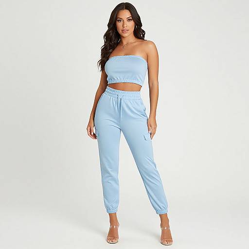 Photograph of a curvy woman with long black hair, wearing a light blue strapless top and matching high-waisted pants, standing against a