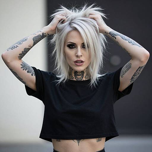 Photograph of a pale-skinned, tattooed woman with platinum blonde spiky hair, wearing a black crop top, hands in hair, intense gaze