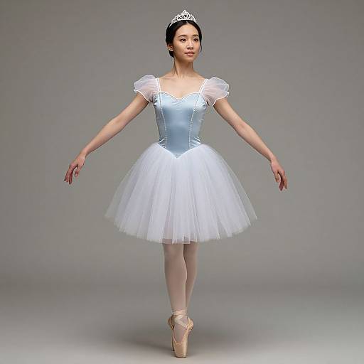 Photograph of an Asian ballerina in a silver-blue bodice and white tulle tutu, wearing a silver tiara and pointe shoes