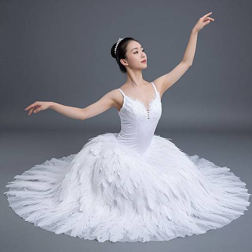 Photograph of an elegant Asian ballerina in a white, feathered, sleeveless ball gown, gracefully posing with arms extended against a gray background