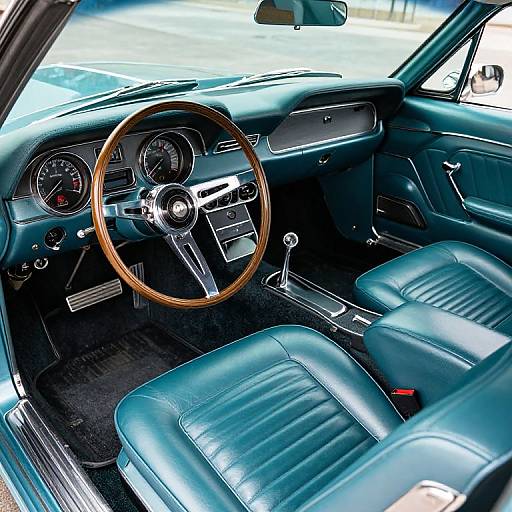 Photograph of a vintage car's interior with teal leather seats, wooden steering wheel, black dashboard, and classic instrument panel.
