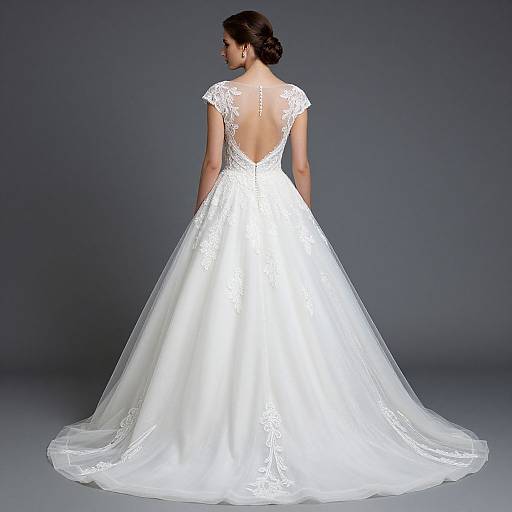 Photograph of a woman in a white, lace-embellished, backless, ball-gown wedding dress with a long train, viewed from