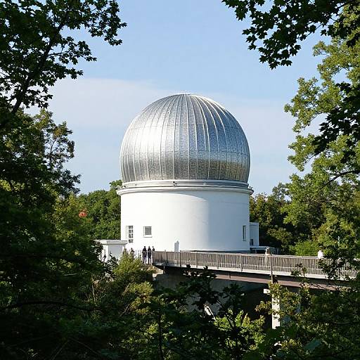 Photograph of a silver-domed white observatory building surrounded by lush green trees under a clear blue sky.