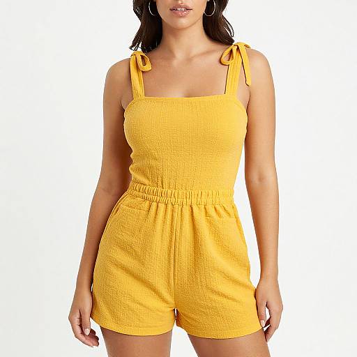 Photograph of a woman wearing a bright yellow, sleeveless romper with side ties, standing against a white background.